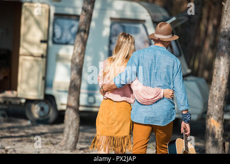 back view of hippie couple hugging and holding guitar near campervan Stock Photo