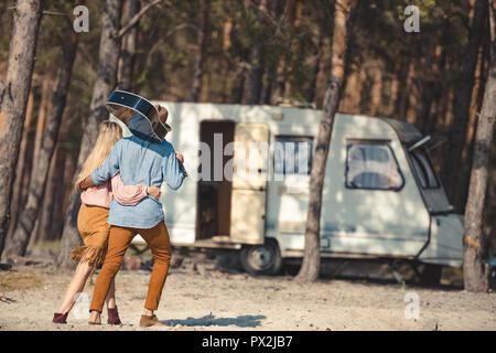 back view of couple hugging and walking with acoustic guitar to campervan in forest Stock Photo