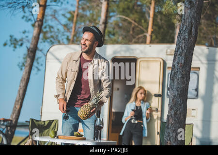 selective focus of man cutting pineapple while woman with wine standing at trailer behind Stock Photo