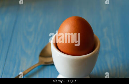 Boiled egg in a white egg cup with spoon on a blue background Stock Photo
