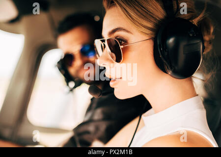 side view of attractive woman in sunglasses and headset sitting near male pilot in cabin of airplane Stock Photo