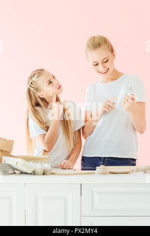 beautiful mother and daughter in white t-shirts cooking together isolated on pink Stock Photo