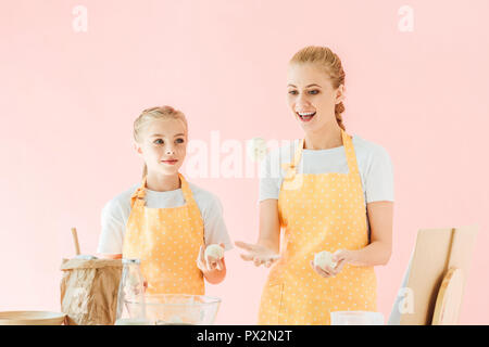smiling mother and daughter juggling with dough pieces while cooking isolated on pink Stock Photo