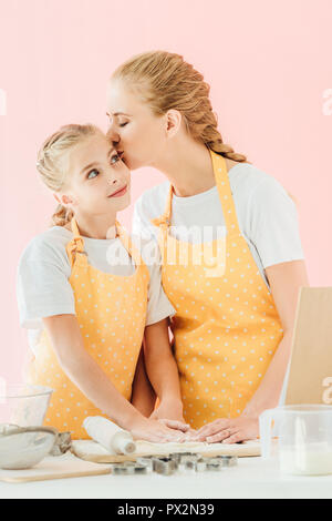 mother kissing her daughter while preparing dough isolated on pink Stock Photo