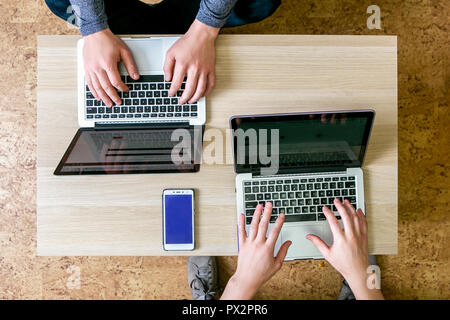 Two young people working on laptops in the office, writing a program, correct the text. Sit at the table opposite each other, top view, close-up Stock Photo
