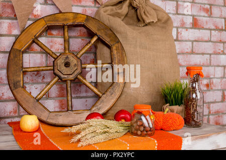 Autumn decoration with red maple leaves, autumn flowers and halloween pumpkins. Fall harvest on brick wall . For holiday post card.Country house design cart wheel, grain bag, nuts, wheat, rye, carpet, thanksgiving day Stock Photo