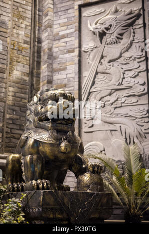 Lion bronze statue at with a dragon fresco on a brick wall at night in a chinese street in Chengdu, China Stock Photo