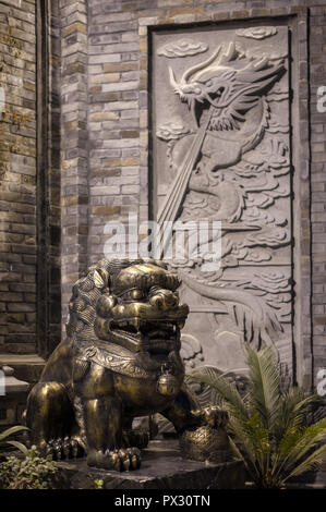 Lion bronze statue at with a dragon fresco on a brick wall at night in a chinese street in Chengdu, China Stock Photo