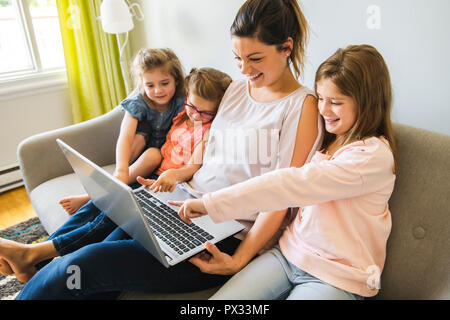 mother and daughters on sofa at home using laptop Stock Photo