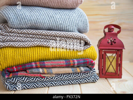 Winter and fall cozy sweaters stack, woolen sweaters and blankets still life with air freshener Stock Photo