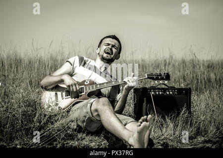 the young man on the field, the musician with the guitar and amp, the emotions of the musician, the concept of music and art Stock Photo