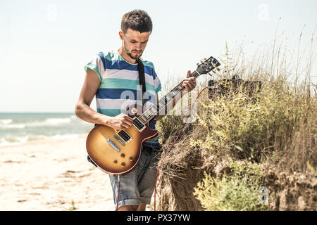 the young man on the field, the musician with the guitar and amp, the emotions of the musician, the concept of music and art Stock Photo