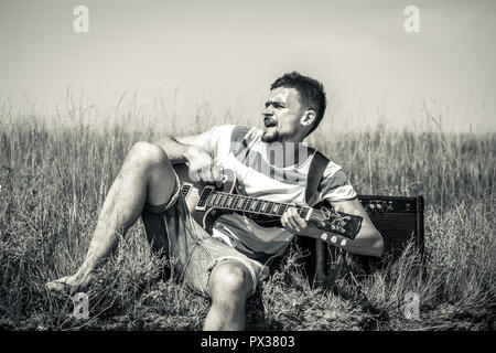 the young man on the field, the musician with the guitar and amp, the emotions of the musician, the concept of music and art Stock Photo