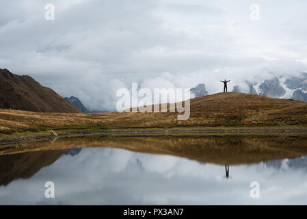 Koruldi lake with a mirror reflection of clouds. View of the Caucasus Mountains. Hiker stands on top of the hill. Samegrelo-zemo svaneti, Georgia Stock Photo