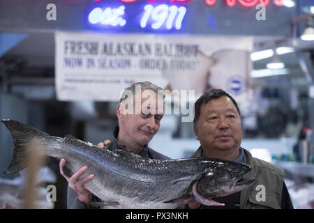Seattle, Washington, USA. 6th Oct, 2018. A seafood stall attendant poses for a photo with a large fish and a tourist in the Pike Place Market in downtown Seattle, Washington, on October 6, 2018. (Credit Image: © Alex EdelmanZUMA Wire) Stock Photo
