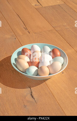 a bowl of various coloured eggs on a wooden surface Stock Photo