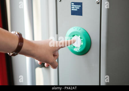 The person presses the stop button in the train. The inscription in German language is translated - STOP. Above the inscription is translated - Continue to press the button. Stock Photo
