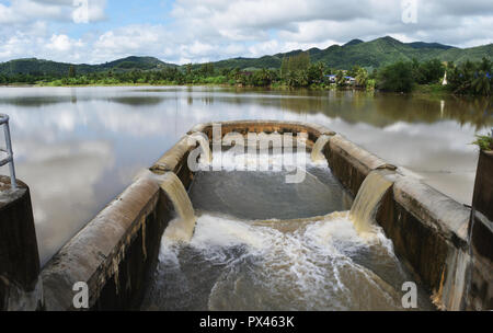Turbid water in the dam overflows into the spillway, The sky with the mountain and the green forest reflect on the water  , Thailand Stock Photo