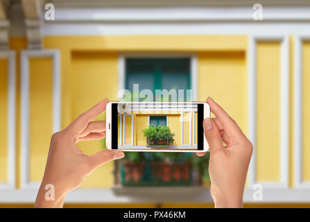A tourist is taking a photo of the window of one of the houses in the center of Milan is shuttered and decorated with flowers on a mobile phone Stock Photo