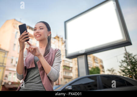 Template of a young beautiful asian woman using an application in her smart phone in front of a blank billboard. Communicate inside the copy space Stock Photo