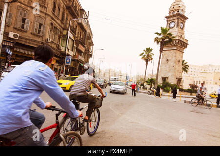 Aleppo, Aleppo Governorate, Syria : People cycles past the baroque clock tower at the Bab al-Faraj neighbourhood of the New City. Stock Photo