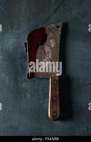 high angle view of an old and rusty meat cleaver full of blood, placed on a dark green rustic surface Stock Photo