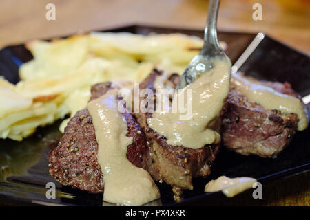 Adding thick peppercorn sauce for steaks. Gratin potatoes on background. Stock Photo