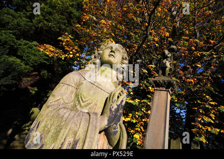 A statue of a praying woman stands out against the autumnal trees in the background on a sunny day in Dean cemetery in Edinburgh Stock Photo