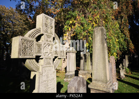 The afternoon sun illuminates some of the gravestones with the trees in the background starting to show signs of an autumnal change in Dean cemetery Stock Photo