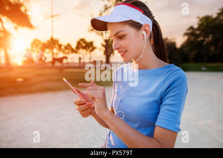 Beautiful young woman is using an app in her smartphone device to play a mobile game in the park Stock Photo