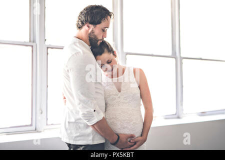 A Handsome man and his beautiful pregnant wife standing near the window at home Stock Photo