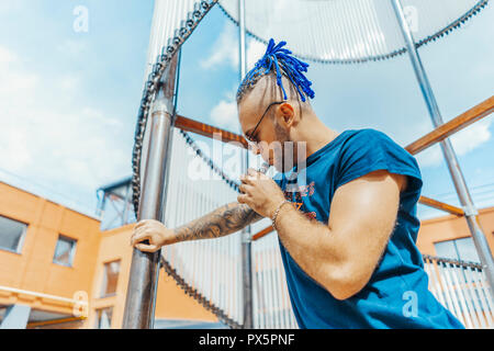Portrait of young vaping man with dreadlocks at art object background. Vapor concept. Vaping e-Cigarette Stock Photo