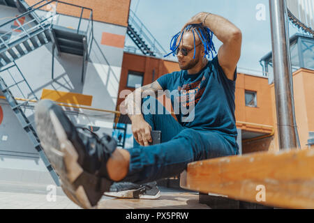 Young attractive man with blue dreadlocks touching his hair. Stock Photo