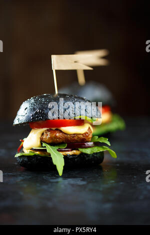Two Black burger with cutlet, greens, cheese, onions and tomatoes on on a dark table Copy space Stock Photo