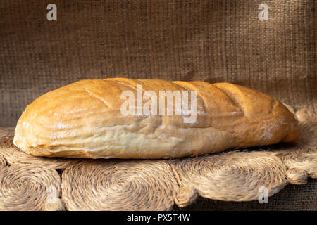 loaf of wheat bread on the background of burlap. Stock Photo