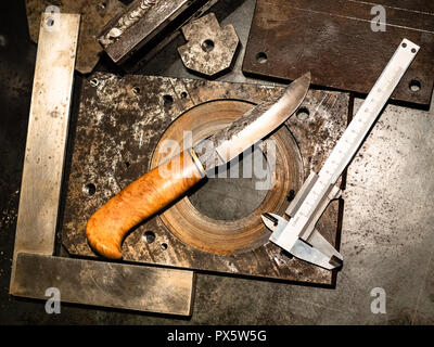 Metalworking still life - top view of forged knife and calliper on metal workbench in turnery workshop in warm yellow light Stock Photo