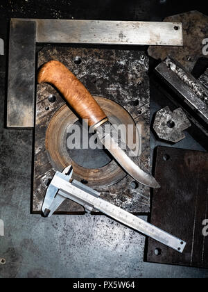 Metalworking still life - top view of forged knife and caliper on metal workbench in turnery workshop in cold blue light Stock Photo