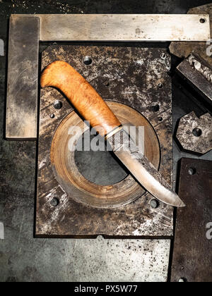 Metalworking still life - top view of forged knife with wooden handle on metal workbench in turnery workshop in warm yellow light Stock Photo