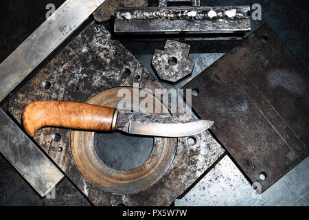 Metalworking still life - top view of forged knife with wooden handle on metal workbench in turnery workshop in cold blue light Stock Photo