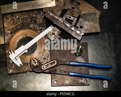 Metalworking still life - top view of callipers and adjustable pliers on metal workbench in turnery workshop in warm yellow light Stock Photo