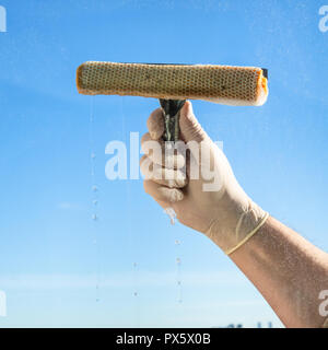 male hand wipes a window glass with blue sky on background Stock Photo