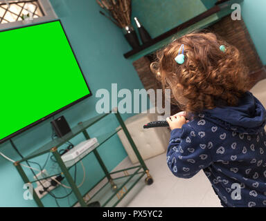 Toddler girl watching television with a remote control. Stock Photo