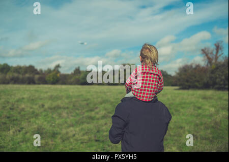 A little toddler is riding on his fathers shoulders in nature Stock Photo