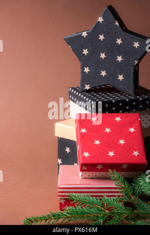Christmas presents frame with a stack of red and black boxes with various designs and a star-shaped gift on top, on a brown background. Stock Photo