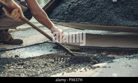 Retro image of two workers working together to lay new asphalt on damaged road with one spreading and arranging the cement mix and the other leveling  Stock Photo