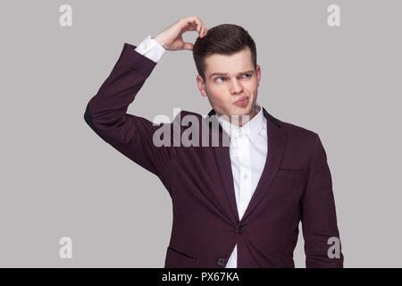 Portrait of thoughtful handsome young man in violet suit and white shirt, standing, looking away and scratching his head with confused face. indoor st Stock Photo