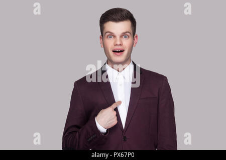 Am I winner?! Portrait of handsome amazed young man in violet suit, white shirt, standing, looking at camera, pointing himself with surprised face and Stock Photo