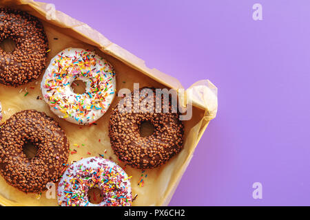 Delicious glazed donuts in box on violet surface. Flat lay minimalist food art background. Top view. Stock Photo