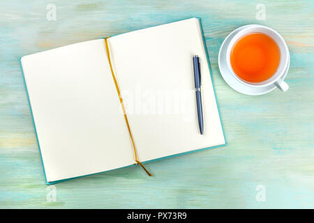 An overhead photo of an open journal notebook with a pen and a cup of tea, shot from above, a diary on a teal blue background with a place for text Stock Photo