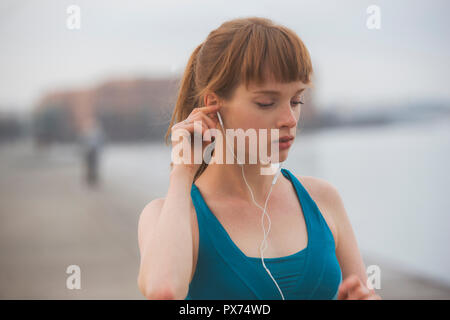 a woman athlete, running by the city seaside, putting on her earphones Stock Photo